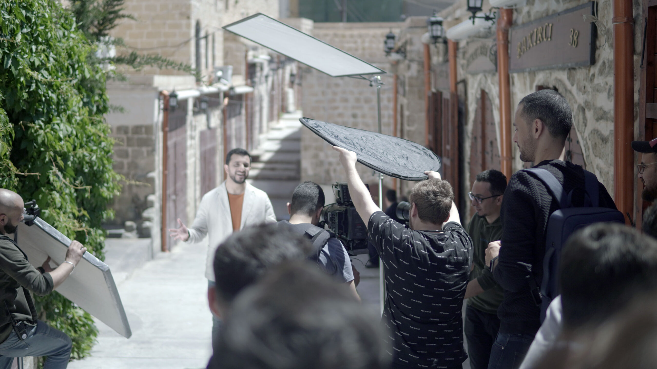 A behind the scenes shot shows a man singing while being filmed