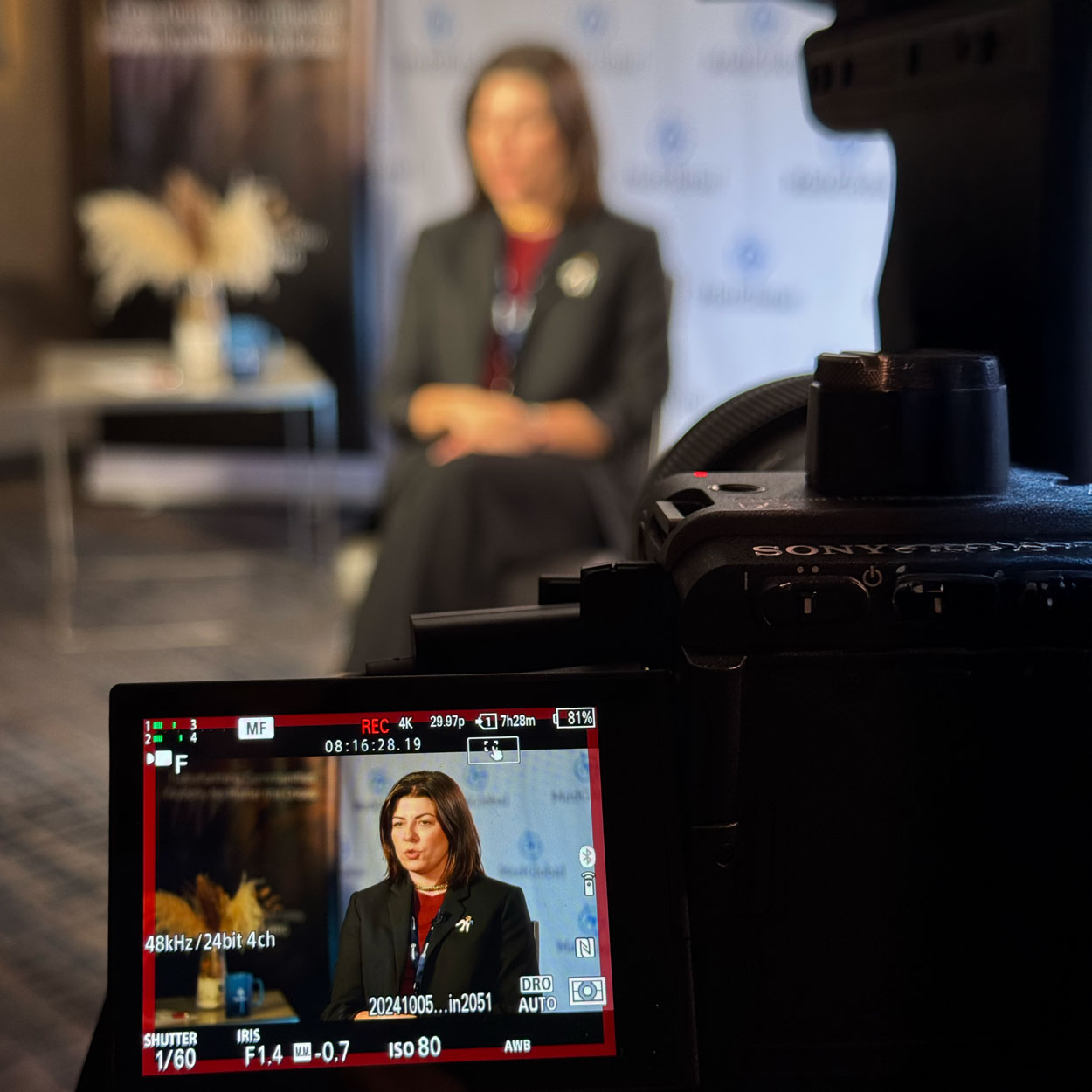 A woman in a red and black suit is shown in the foreground of a camera